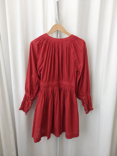 Red pleated dress on a hanger against a white background